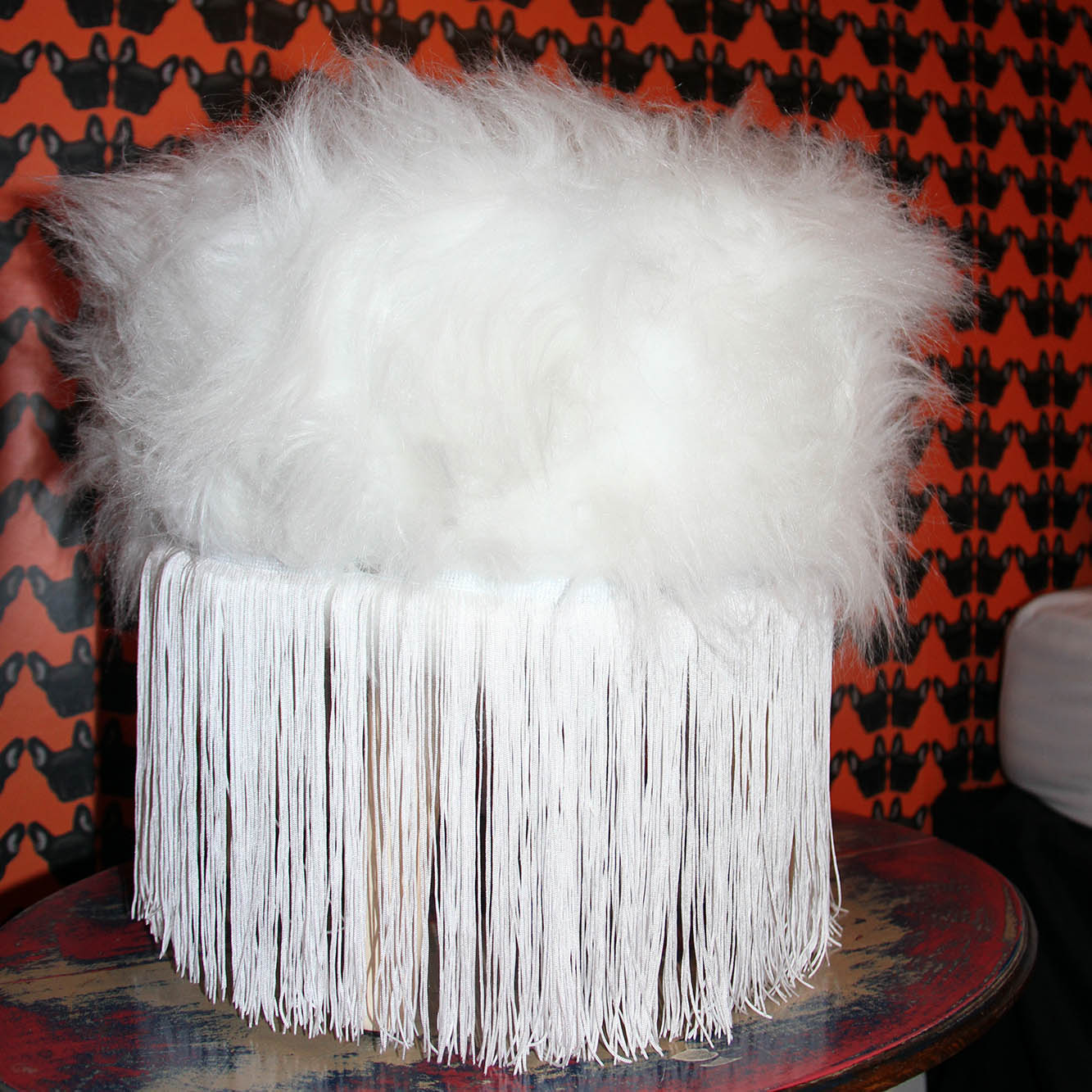 white faux fur and tassel footstool with franchise bulldog wallpaper in the background