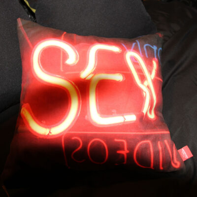 45cm cushion with the word sex in neon lights on it, resting on black sheets
